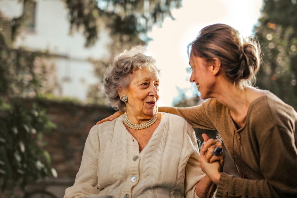 Certificate Courses Elderly woman and adult daughter share a joyful, affectionate moment in a sunny garden.