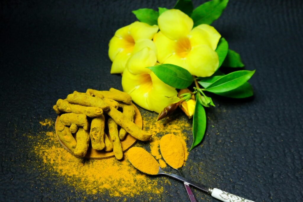Diploma Courses A vibrant display of turmeric root, powder, and yellow flowers on a textured black background.